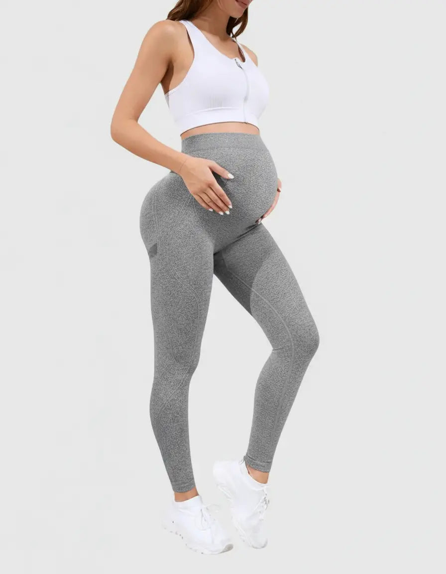 Pregnant woman in gray belly-support sculpting maternity activewear leggings and a white sports bra.
