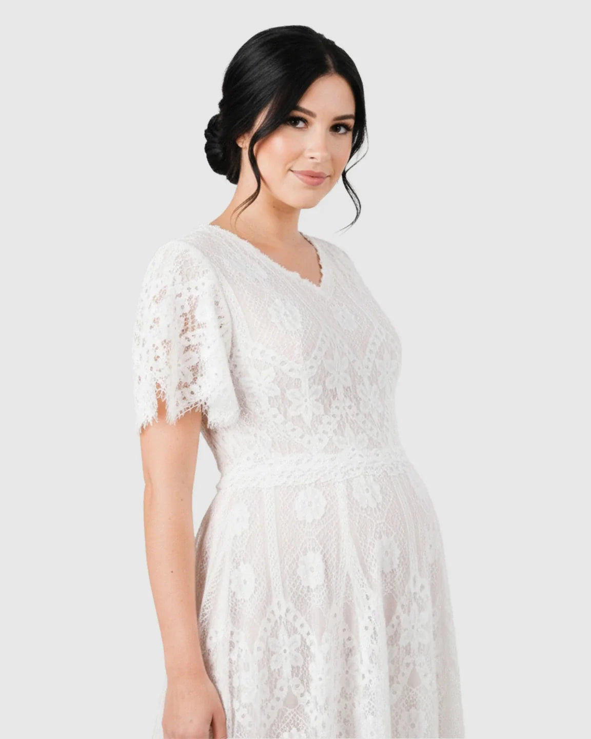 White vintage lace maternity gown with flutter sleeves and V-neck, highlighting a pregnant woman's bump.