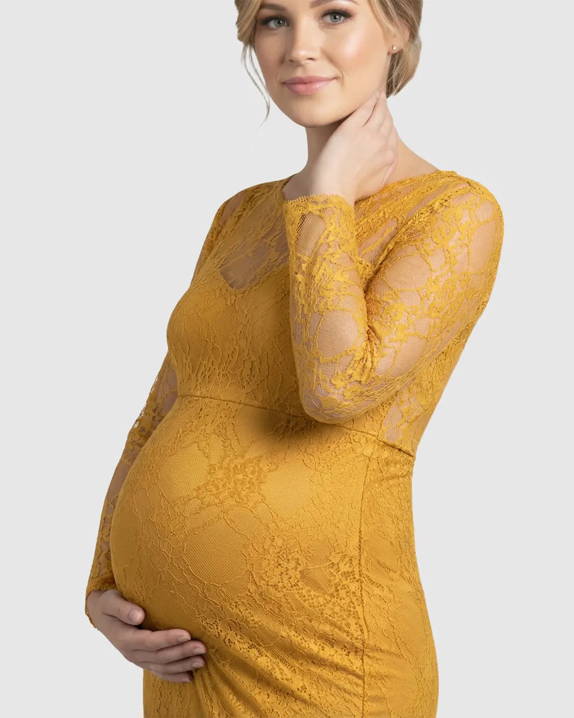 Pregnant woman in a mustard yellow sheer lace trumpet maternity gown with long sleeves, holding her bump.