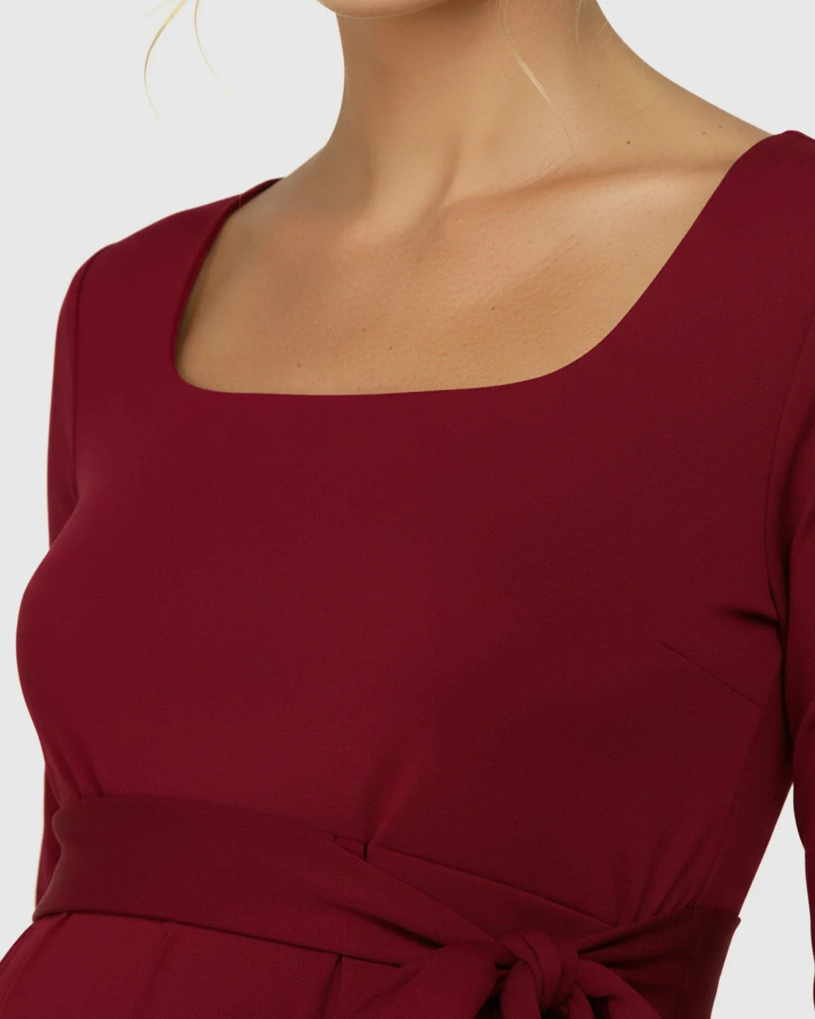 Close-up of a pregnant woman wearing a red square-neck, long-sleeve bodycon maternity midi dress with a side-tie.