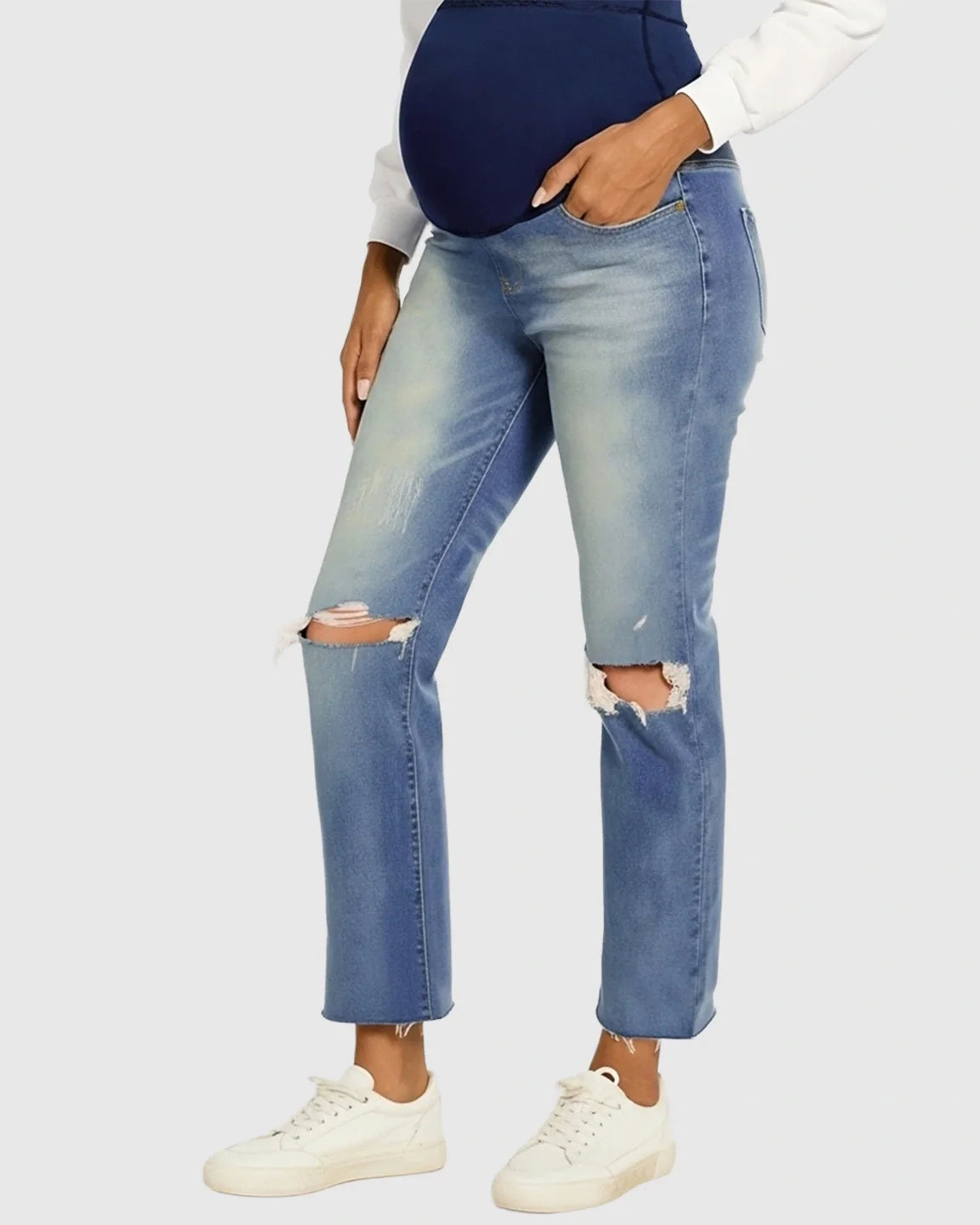 Woman wearing distressed light wash maternity jeans with a navy belly band and white sneakers.