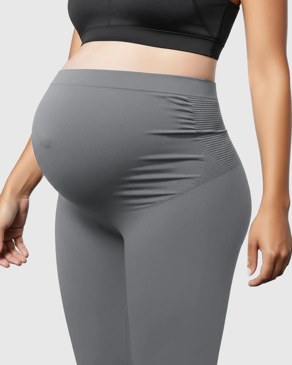Pregnant woman wearing gray high-waist seamless maternity support leggings with ribbed side panels.