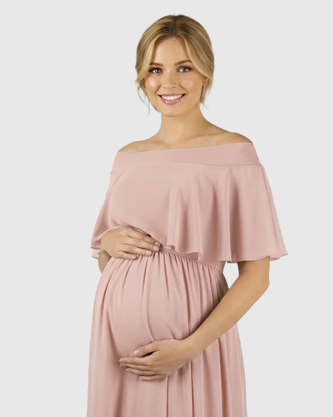 Blonde pregnant woman smiling, wearing a pink chiffon off-shoulder bohemian maternity photoshoot dress.