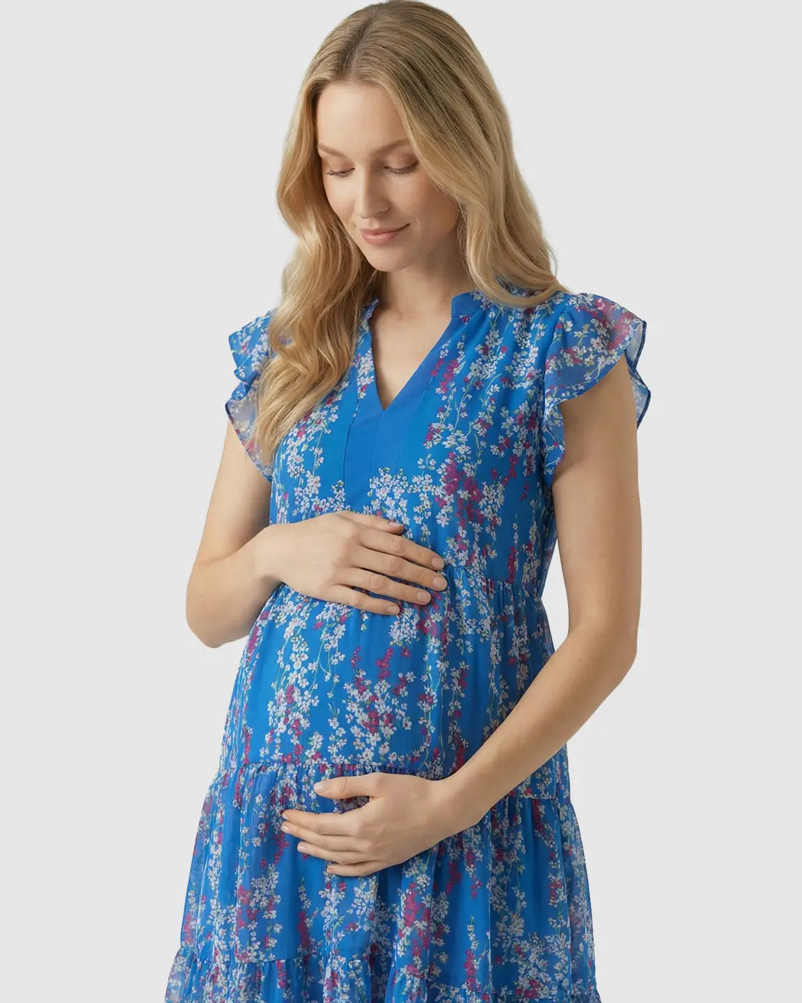 Blonde pregnant woman in a blue floral chiffon V-neck A-line maternity dress with flutter sleeves.