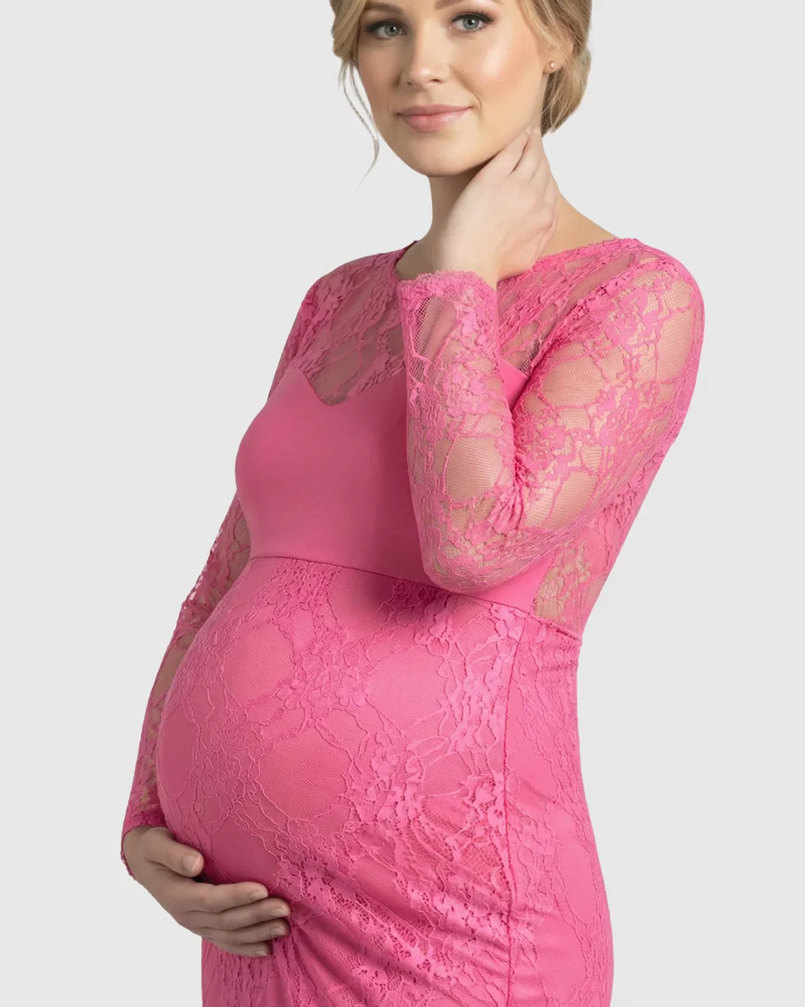Pregnant woman in a sheer pink lace trumpet maternity photoshoot gown with long sleeves, hugging her baby bump.