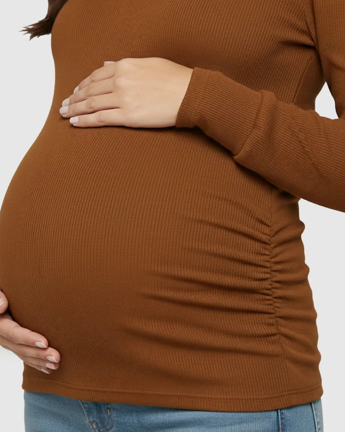 Maternity top in warm brown, ribbed knit with long sleeves and ruched sides, worn by a pregnant woman.