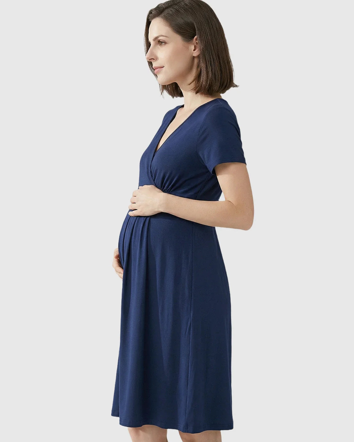 Pregnant woman in a navy V-neck A-line maternity and nursing dress, hands on bump.