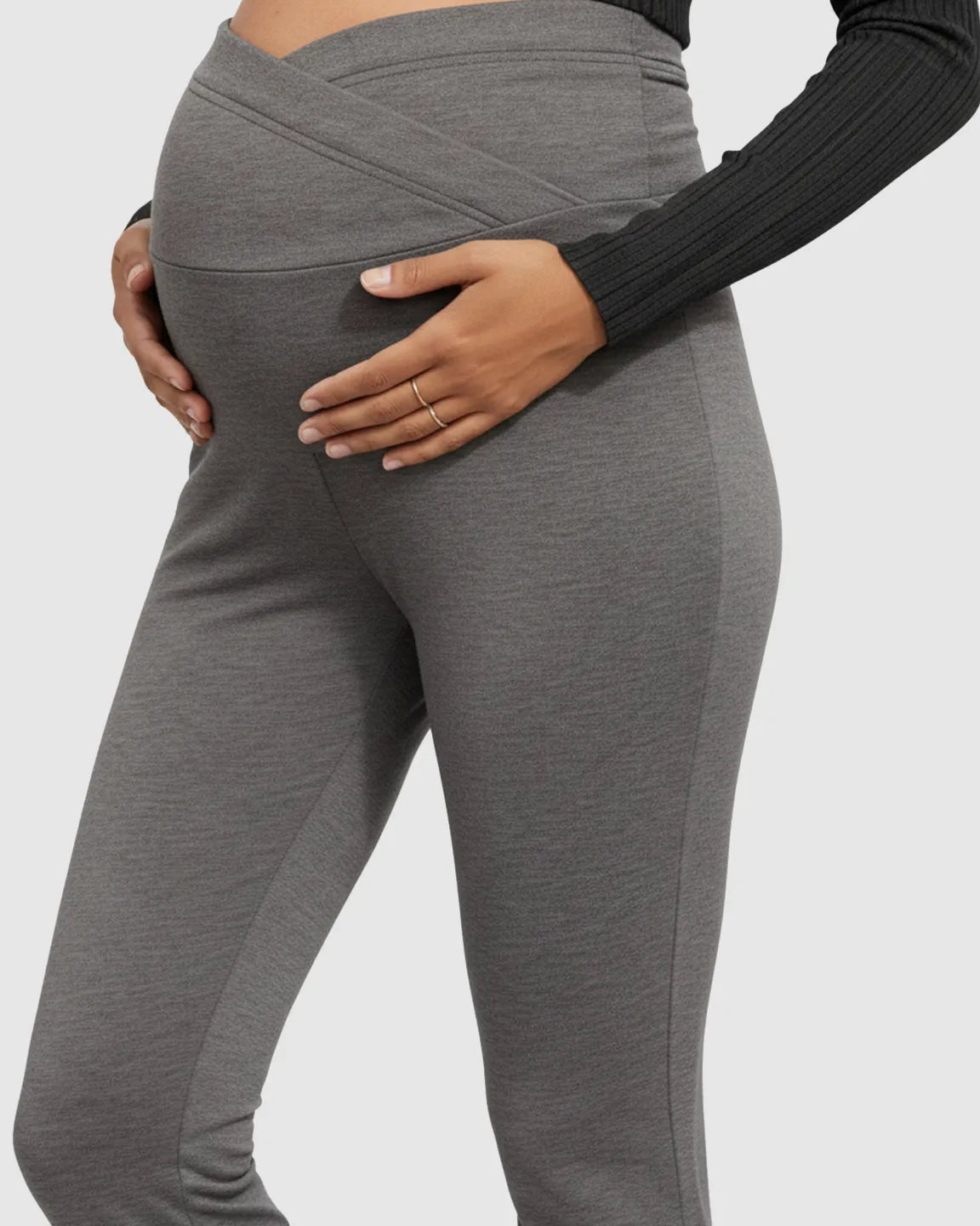 Maternity model in gray crossed waistband flared pants, hands on bump.