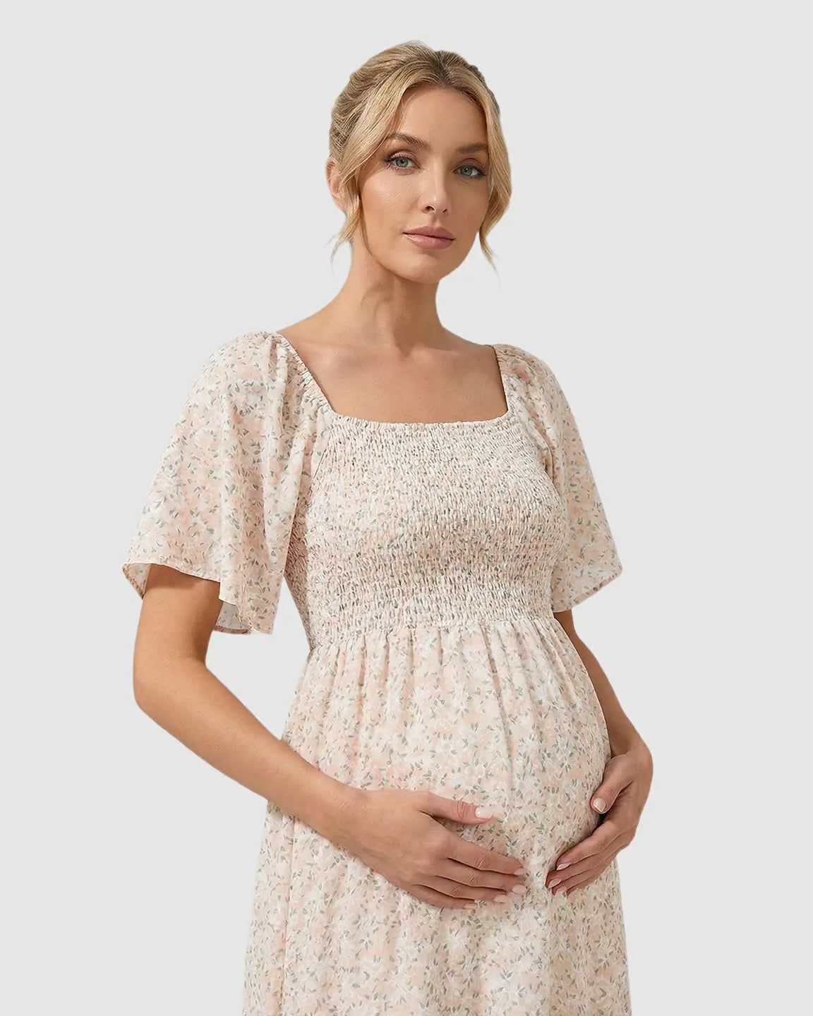 Pregnant woman in a pink floral flutter-sleeve smocked maternity midi dress, hands on belly.