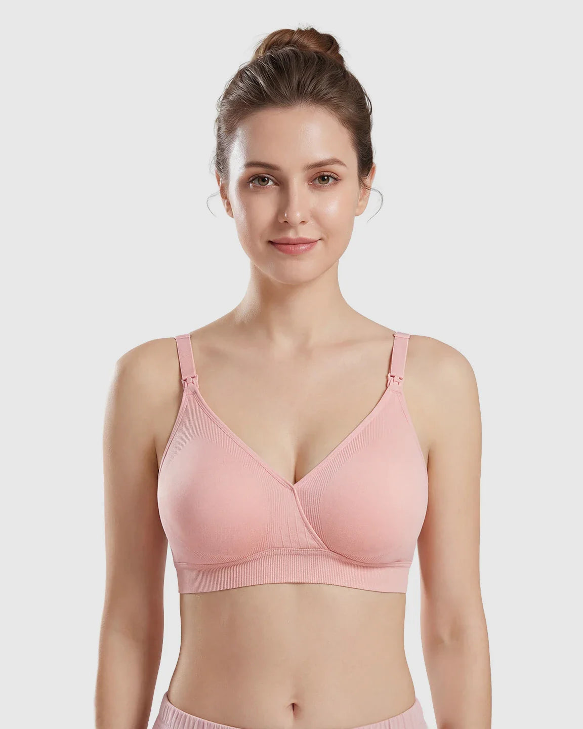 Woman models a pink seamless cross-front wireless nursing bra with adjustable straps and ribbed band.