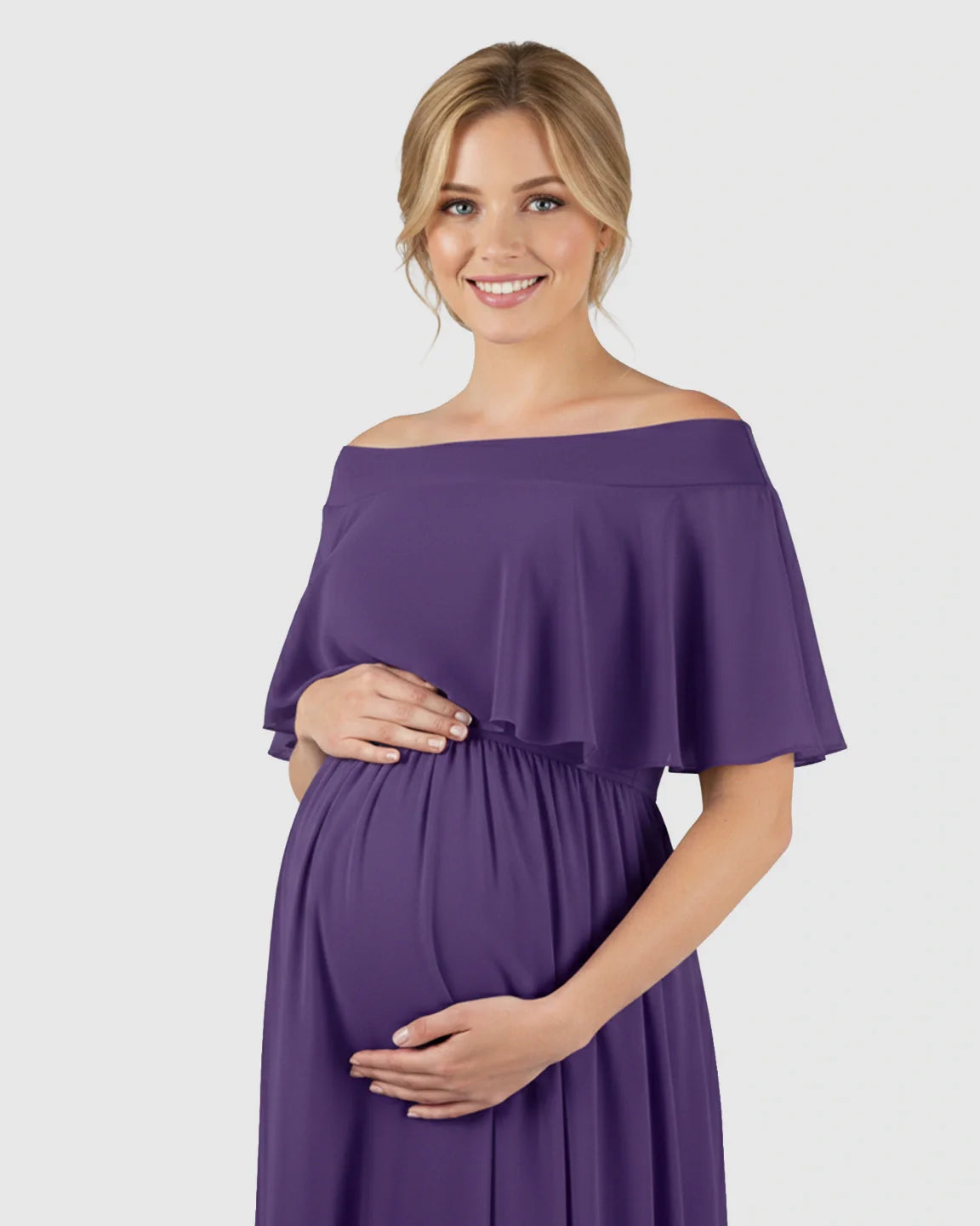 Smiling pregnant woman in a flowing purple off-shoulder chiffon maternity dress, hands cradling her bump.