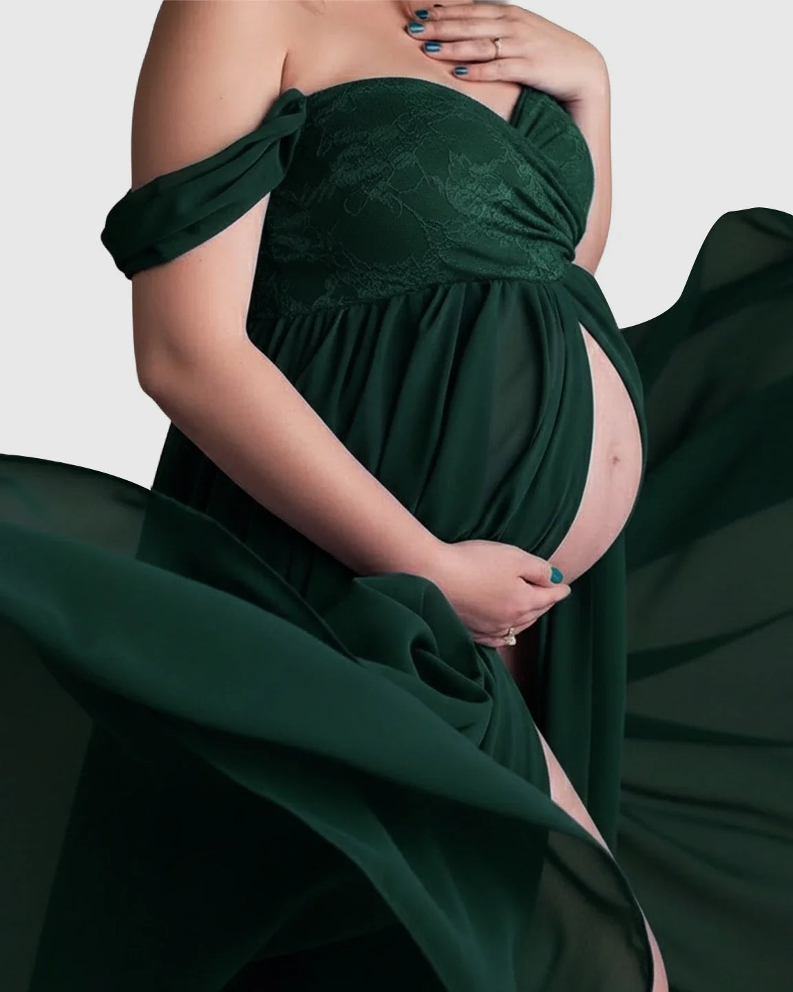 Emerald green off-shoulder chiffon maternity gown with lace bodice and flowing skirt, revealing pregnant belly.