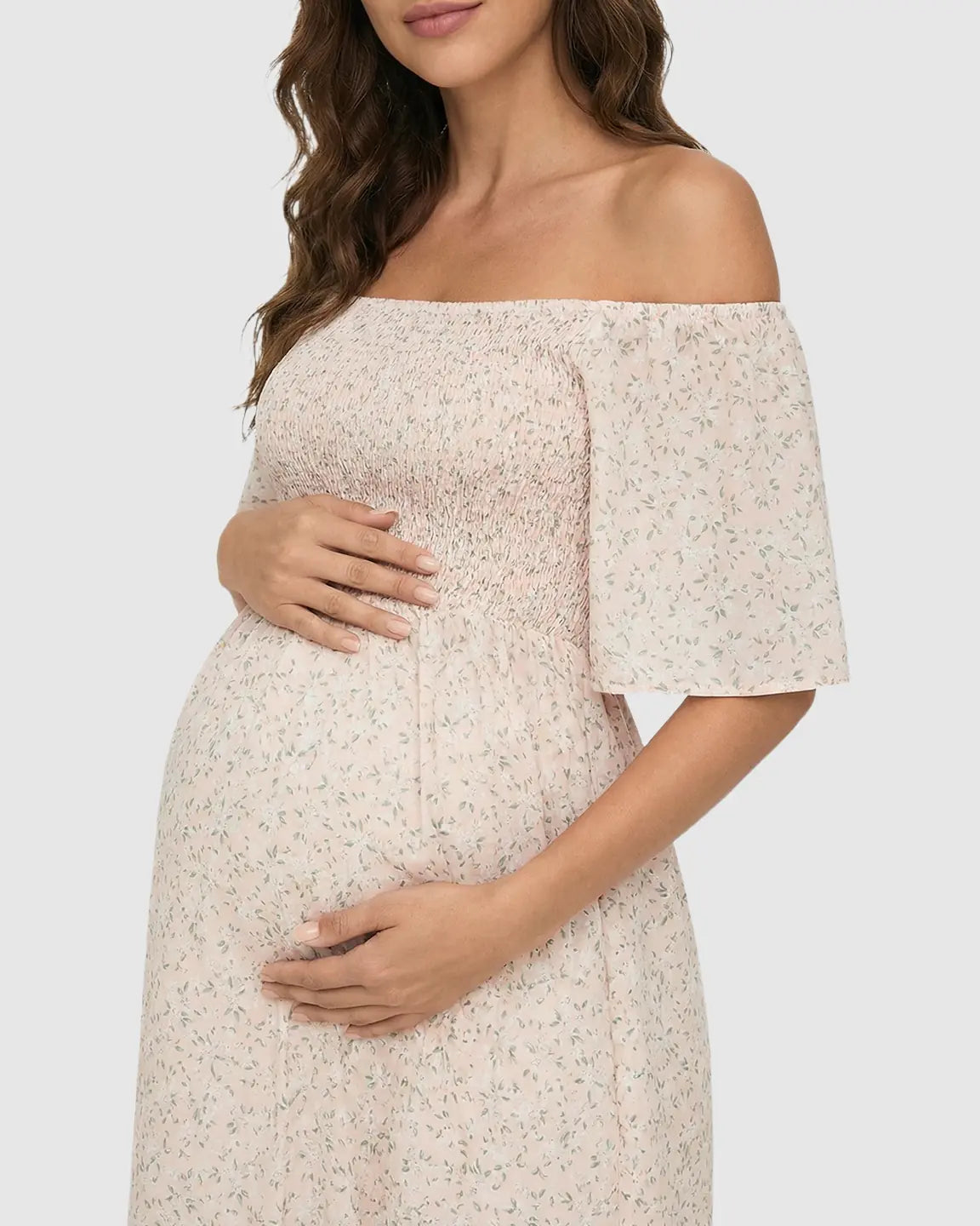 Pregnant woman in a pink floral off-shoulder smocked maternity midi dress with flutter sleeves.