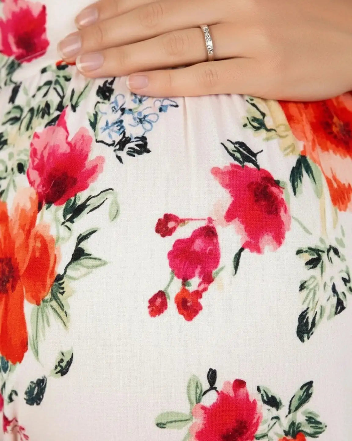 Close-up of a pregnant belly in a white floral maternity maxi dress with red and orange flowers.