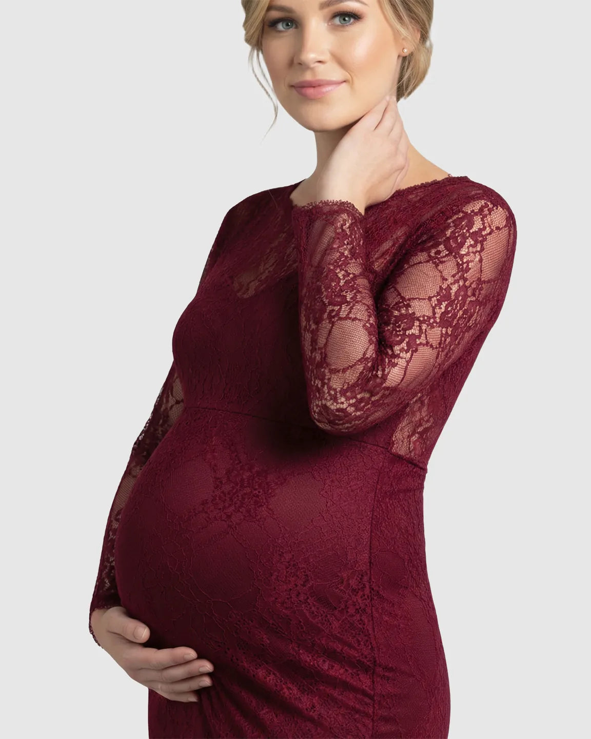 Pregnant woman in a sheer lace trumpet maternity photoshoot gown in a rich burgundy color.