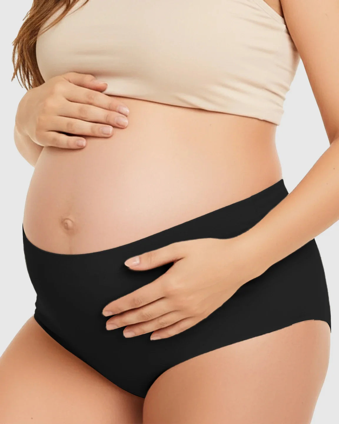 Pregnant woman wearing black seamless high-waist support maternity underwear, gently cradling her belly.