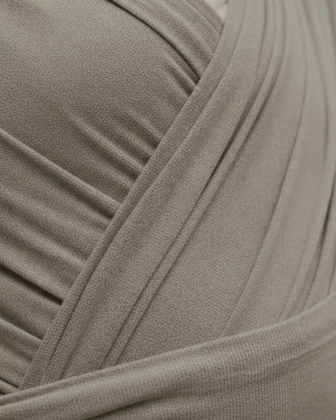 Close-up of a soft, breathable, taupe adjustable wrap-around baby carrier with gentle folds.