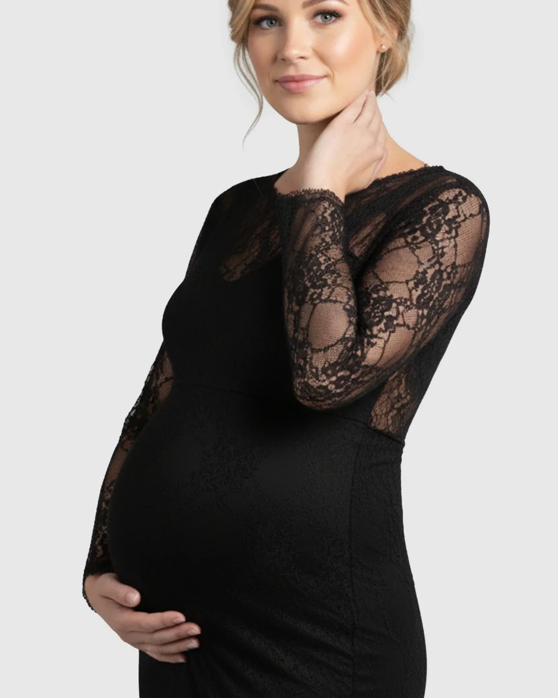 Pregnant woman in a black sheer lace long-sleeve maternity photoshoot gown, gently cradling her baby bump.