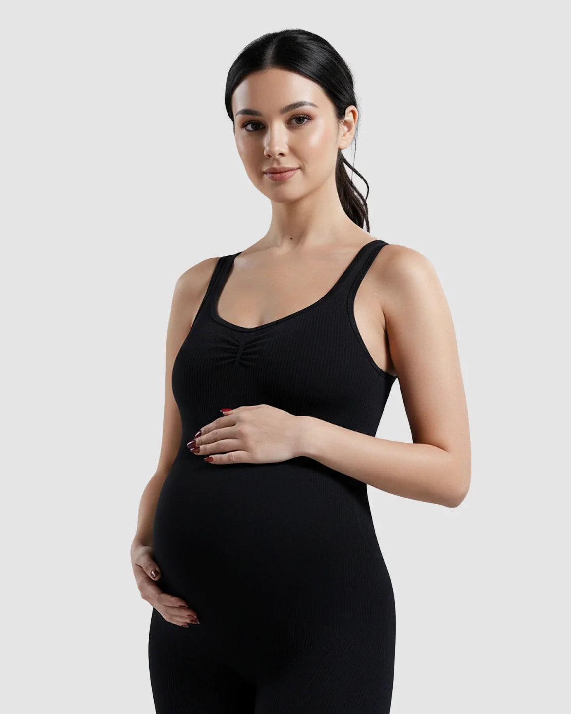 Pregnant woman in a black ribbed high-waisted stretch maternity bodysuit, hands on her bump.
