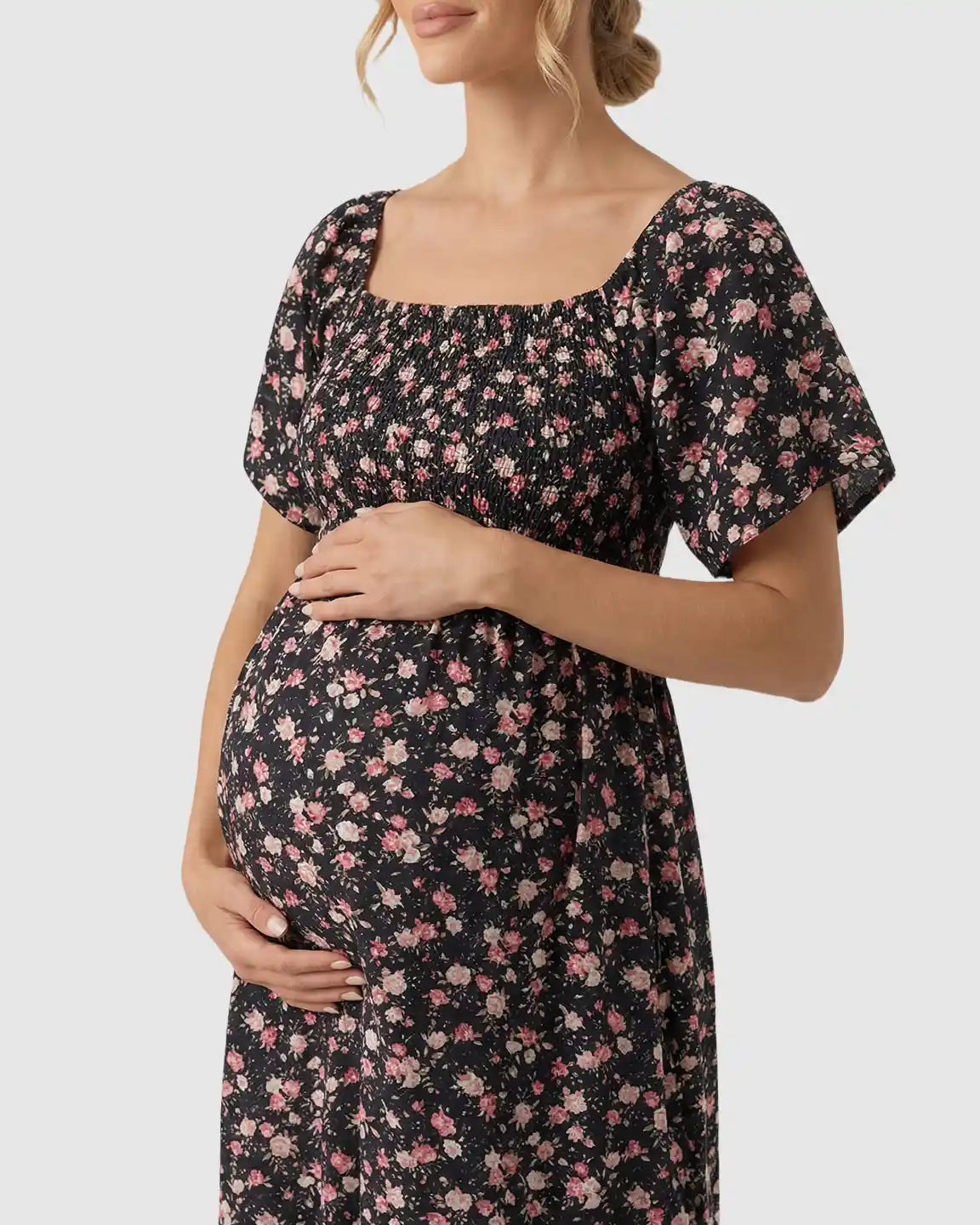 Pregnant woman in a black floral flutter-sleeve smocked maternity midi dress with pink flowers.