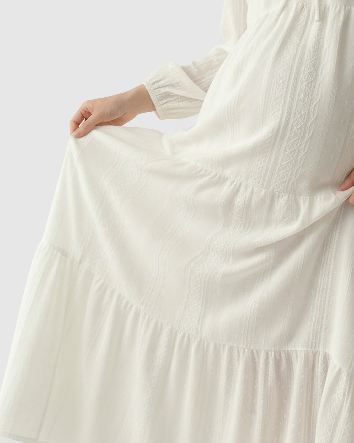 White tiered maternity midi dress with long sleeves and subtle textured fabric.