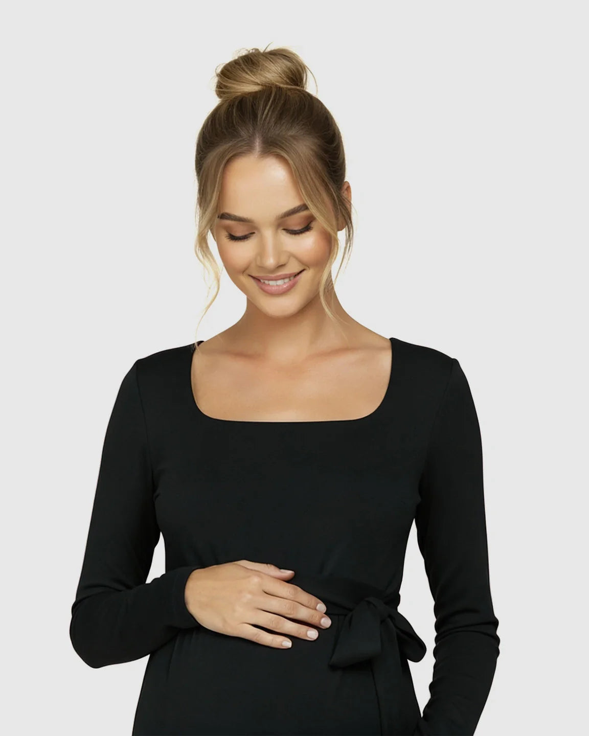 Smiling pregnant woman in a black square neck, long-sleeve, side-tie bodycon maternity midi dress.