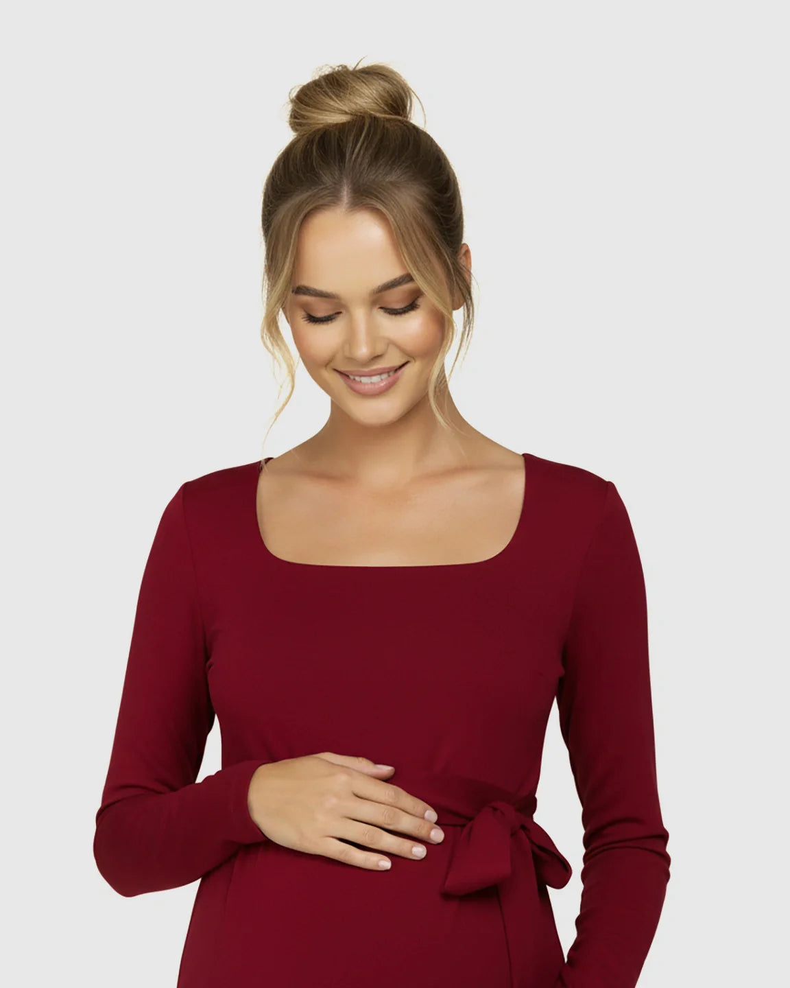 Smiling pregnant woman in a red square neck, long-sleeve bodycon maternity midi dress with a side-tie.