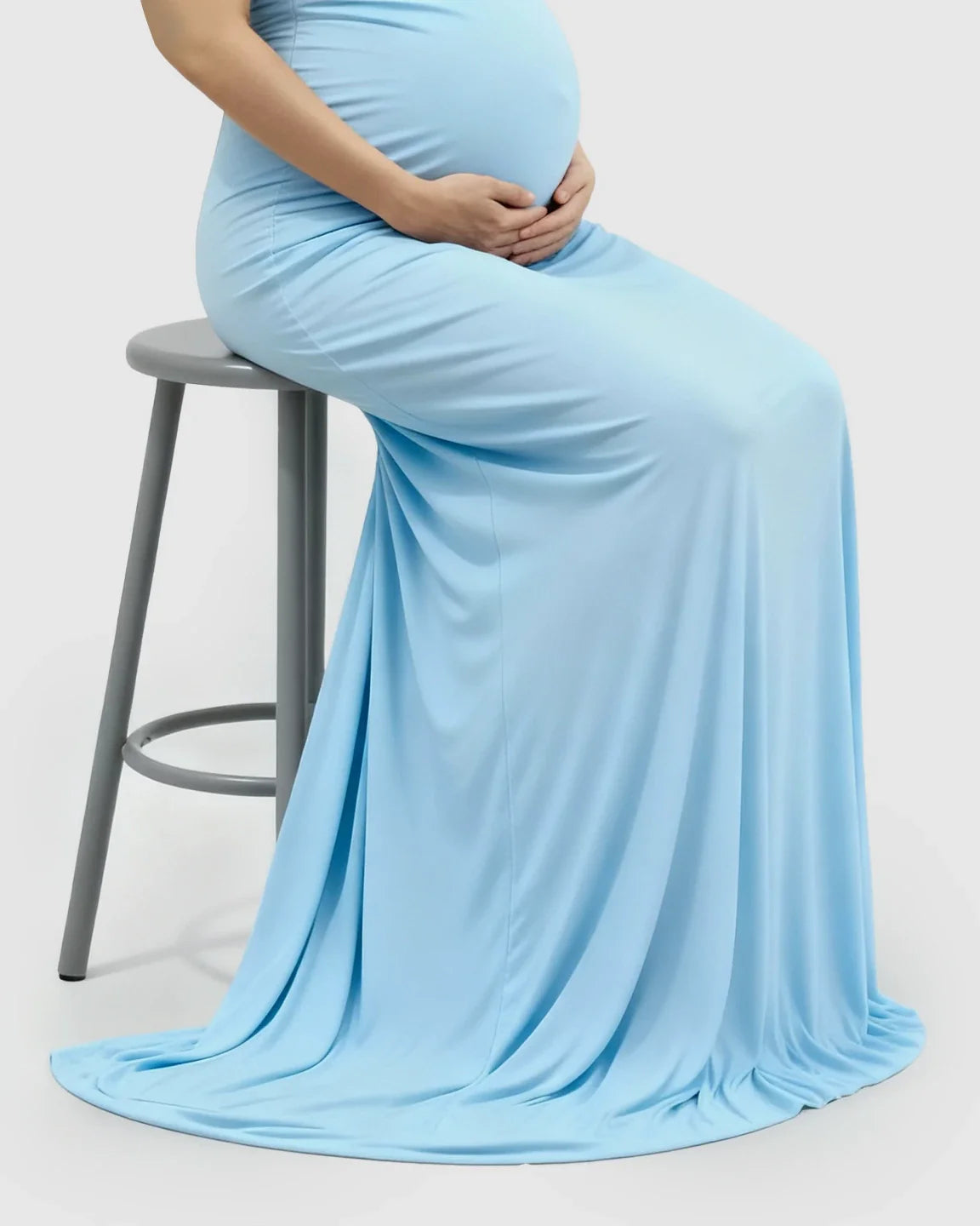 Pregnant woman in a light blue off-shoulder bodycon maternity mermaid gown, seated on a stool.