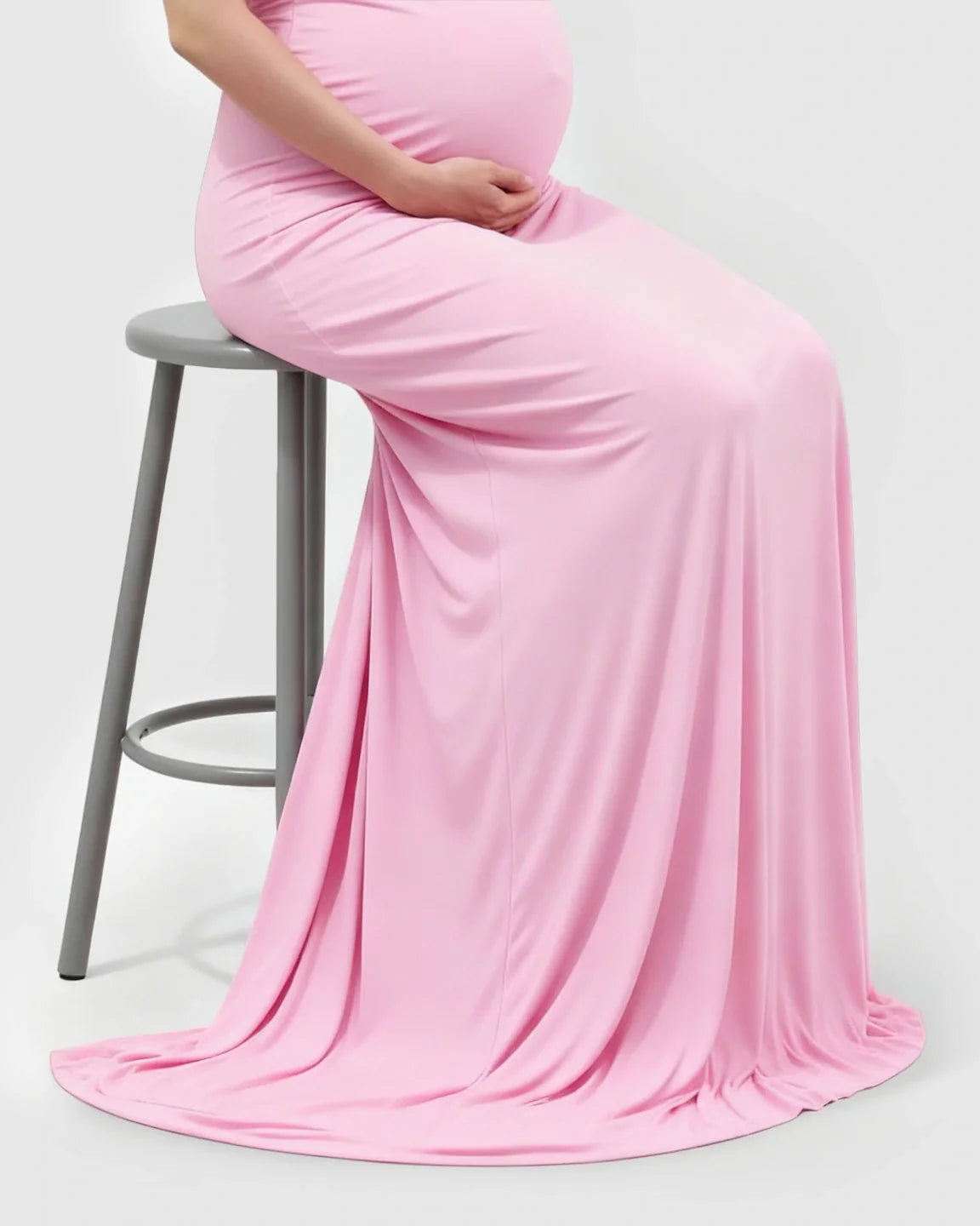 Pregnant woman in a pink off-shoulder bodycon maternity mermaid gown, seated on a stool.
