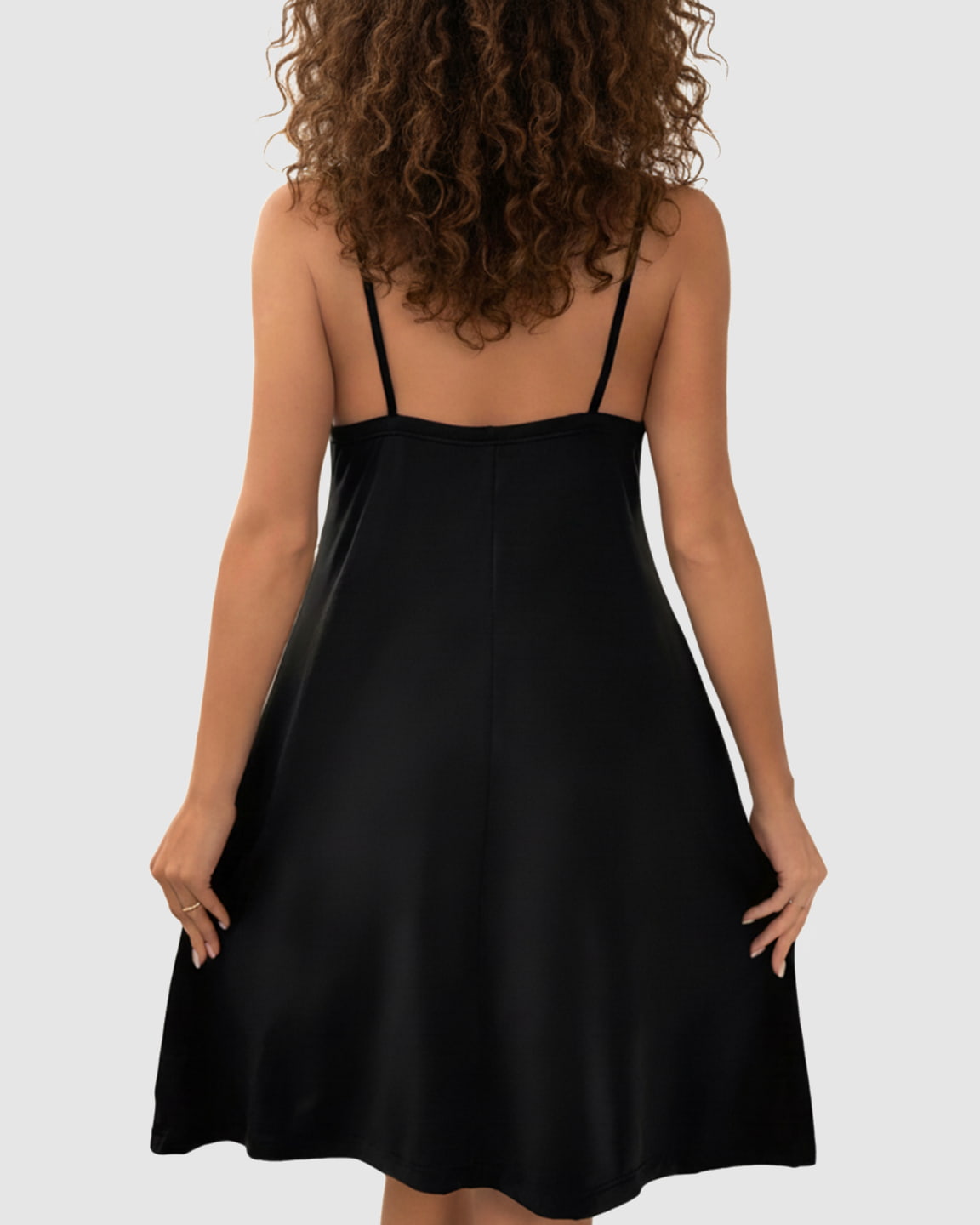 Woman from behind wearing a black thin-strap A-line maternity midi dress, smooth polyester blend.