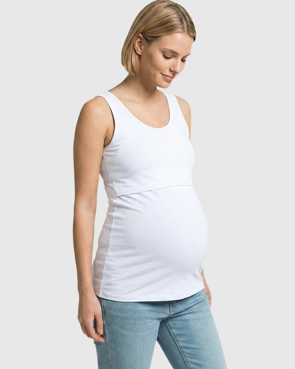 Blonde pregnant woman in a white stretch nursing-access maternity tank top and jeans.