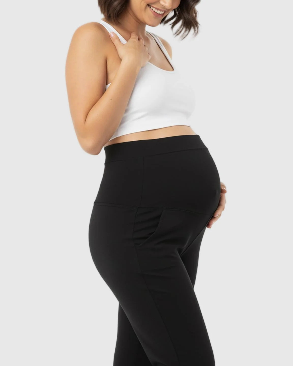 Smiling pregnant woman in black stretch flared maternity pants with pockets and a white crop top.