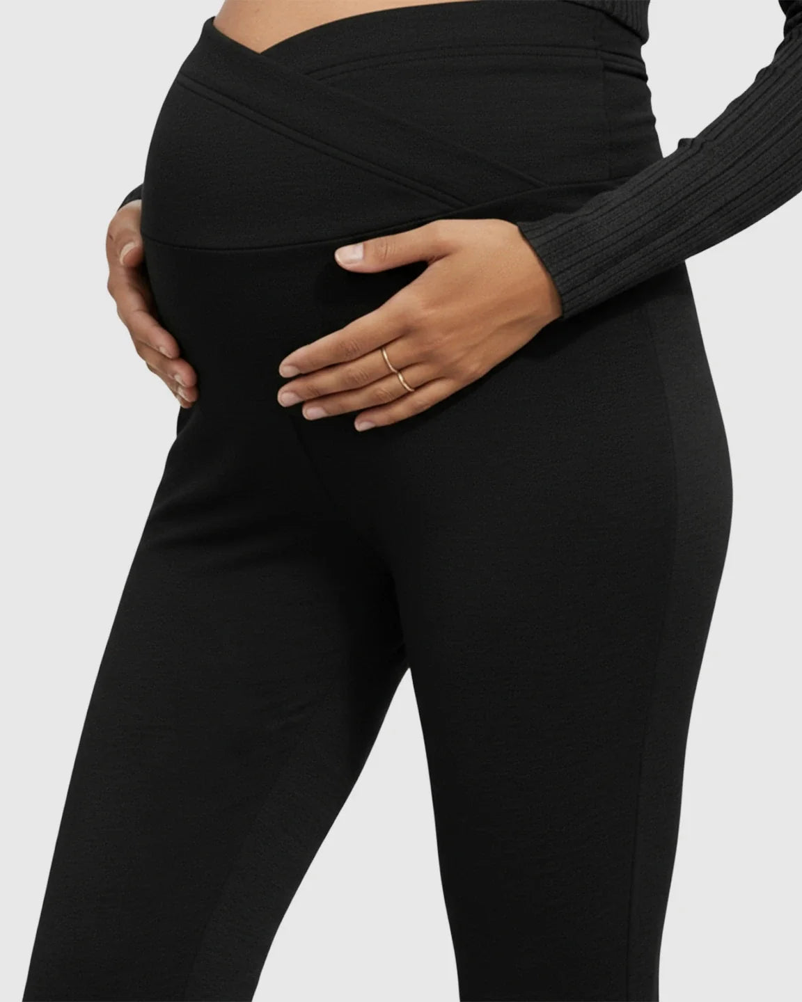 Black flared maternity pants with a crossed waistband, gently hugging a pregnant belly.