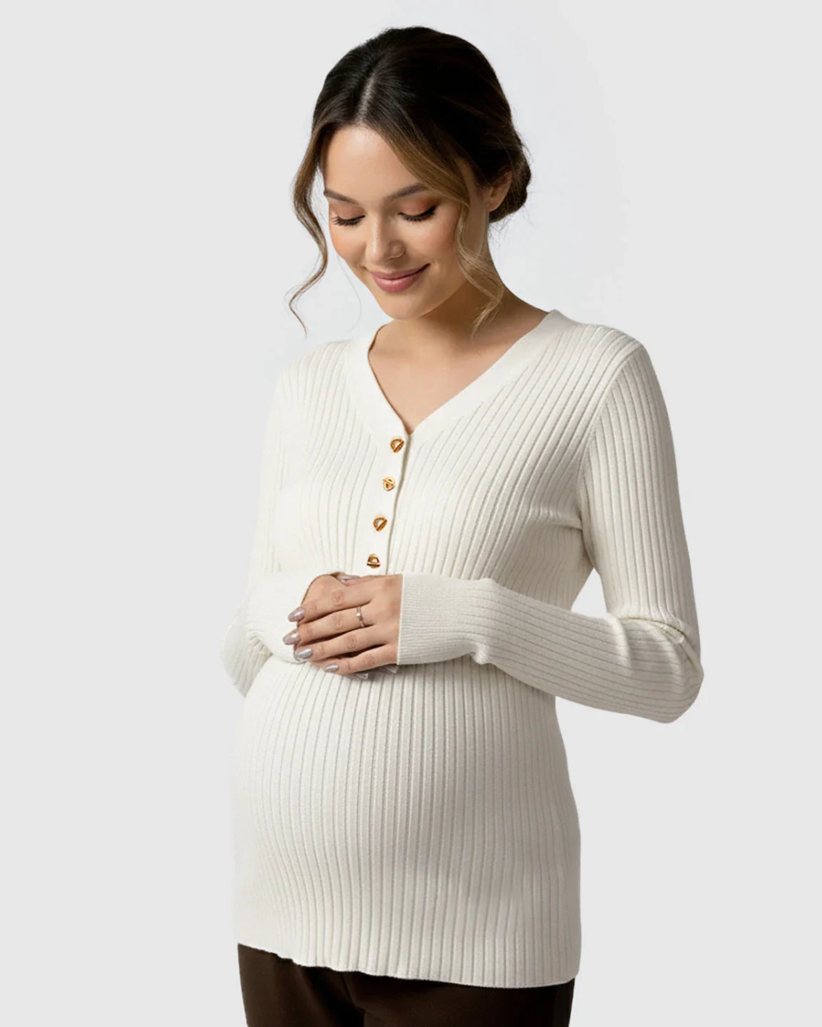 Pregnant woman in a cream ribbed V-neck maternity nursing sweater with gold buttons.