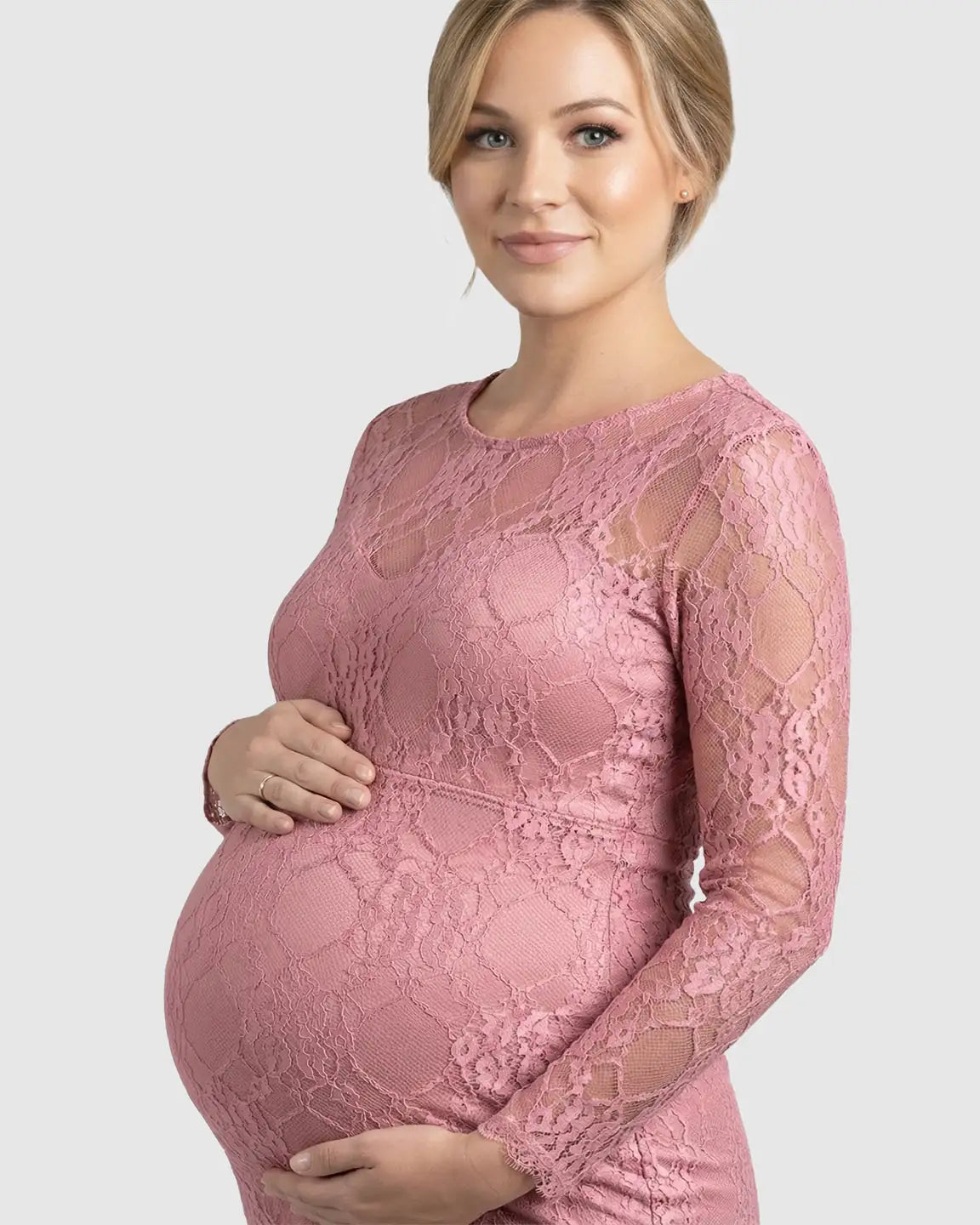 Pregnant woman in a pink sheer lace long-sleeve maternity photoshoot gown, cradling her bump.