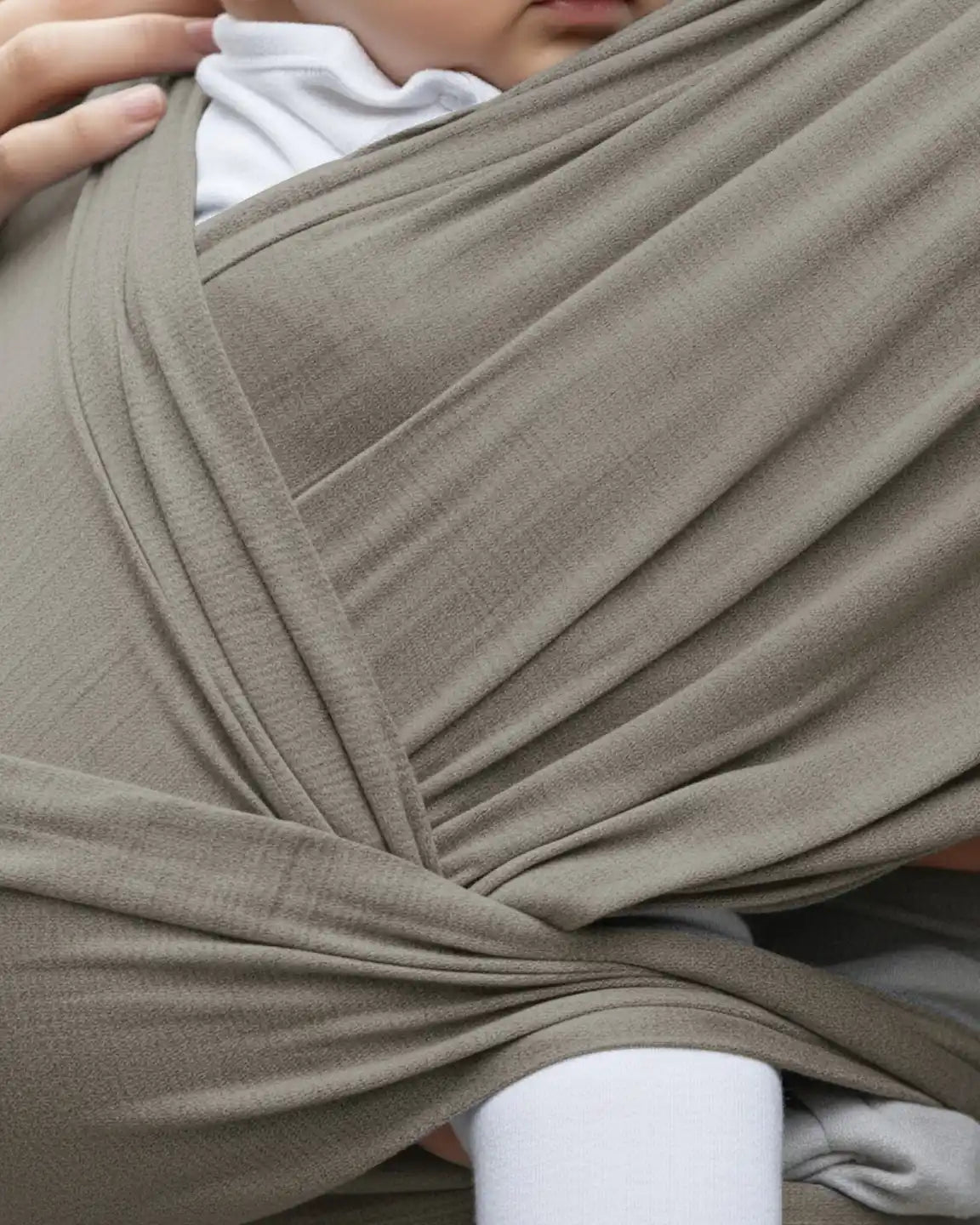Close-up of a baby in a soft, breathable, olive green adjustable wrap-around baby carrier.