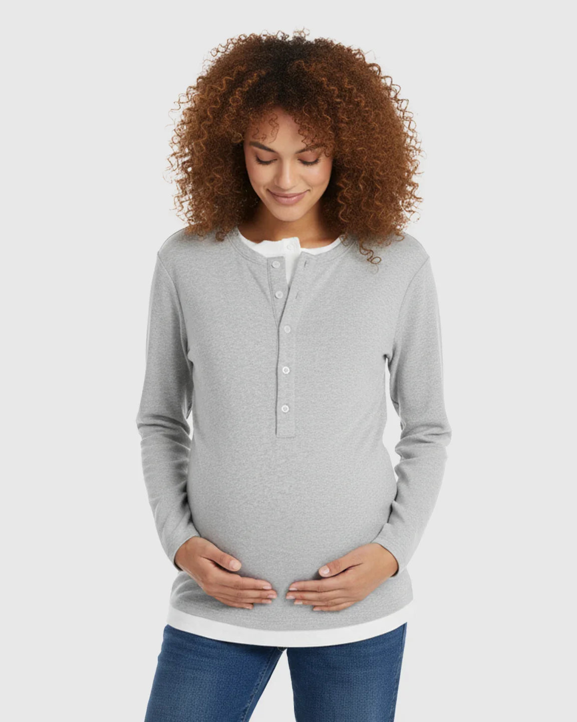 Pregnant woman in a gray long-sleeve Henley maternity and nursing top with white trim, holding her belly.
