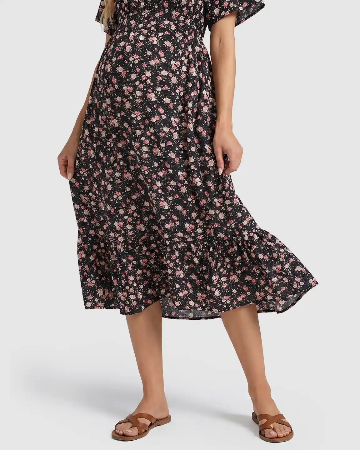 Black floral flutter-sleeve smocked maternity midi dress with pink flowers and tiered skirt, worn with sandals.