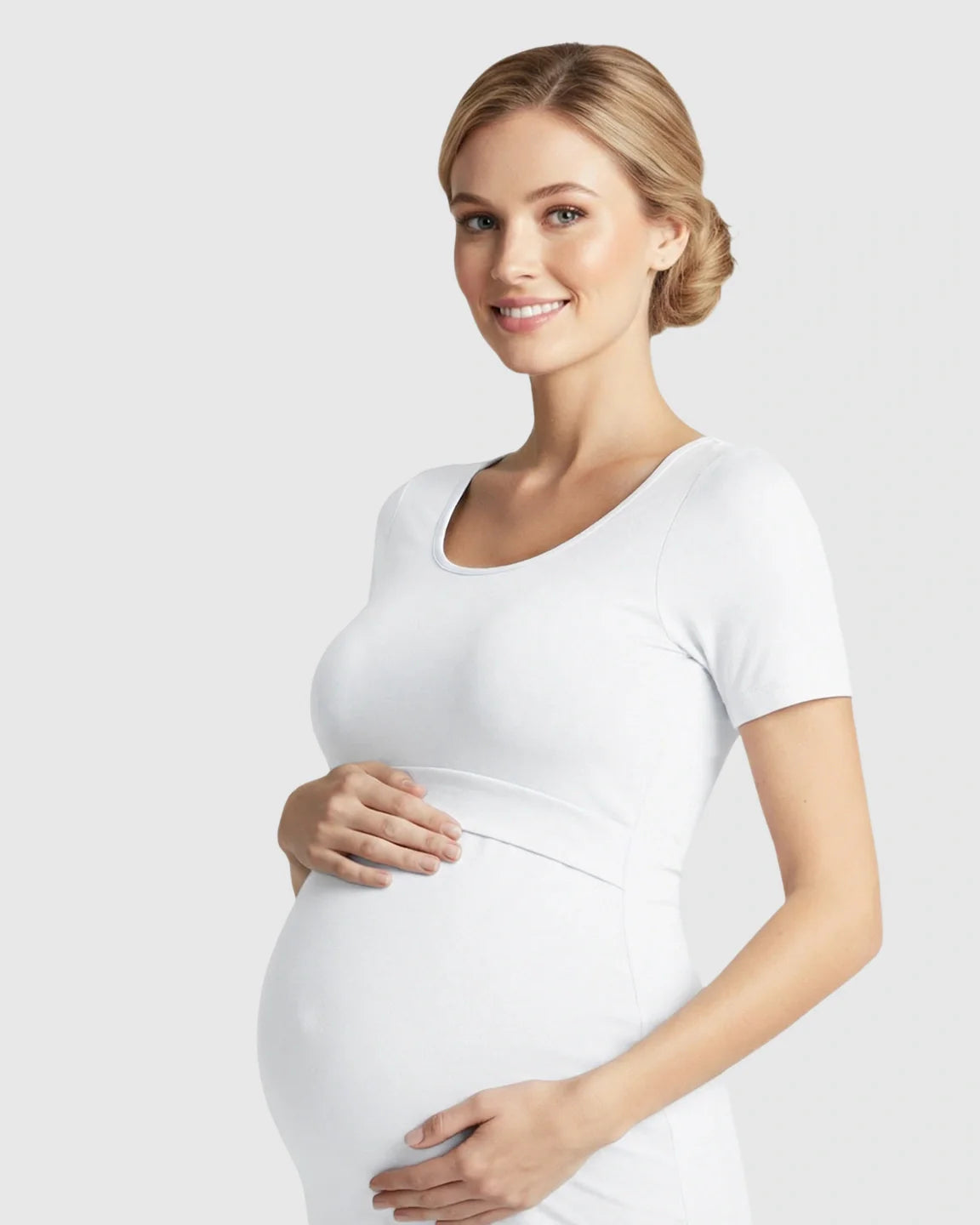 Smiling pregnant woman in a white stretch-fit V-neck nursing t-shirt, cradling her belly.