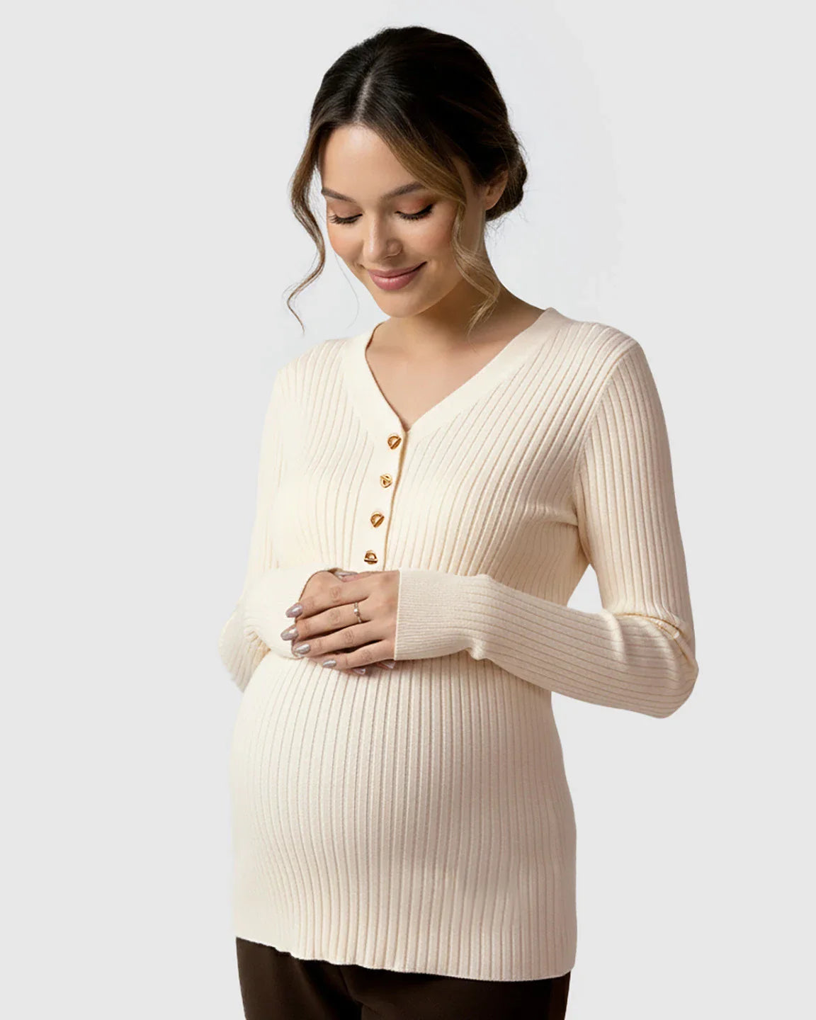 Pregnant woman in a cream ribbed V-neck maternity nursing sweater with gold buttons, holding her belly.