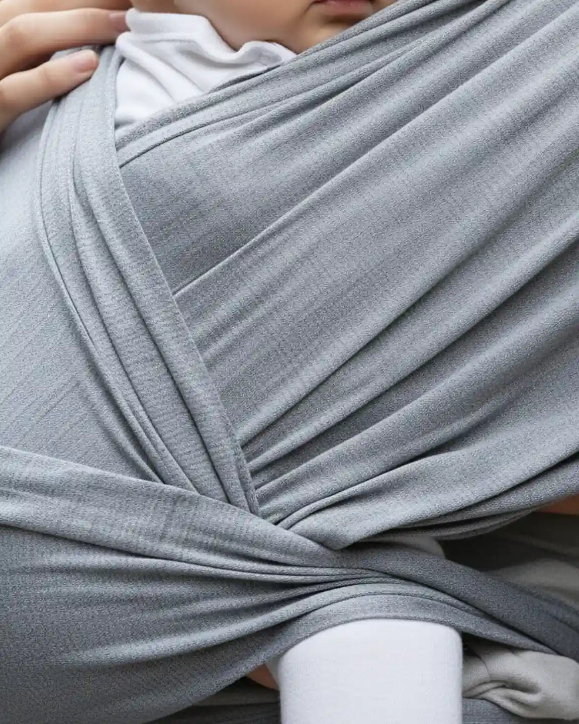 Close-up of a baby in a soft, heather gray adjustable wrap-around carrier, showing the fabric's texture.
