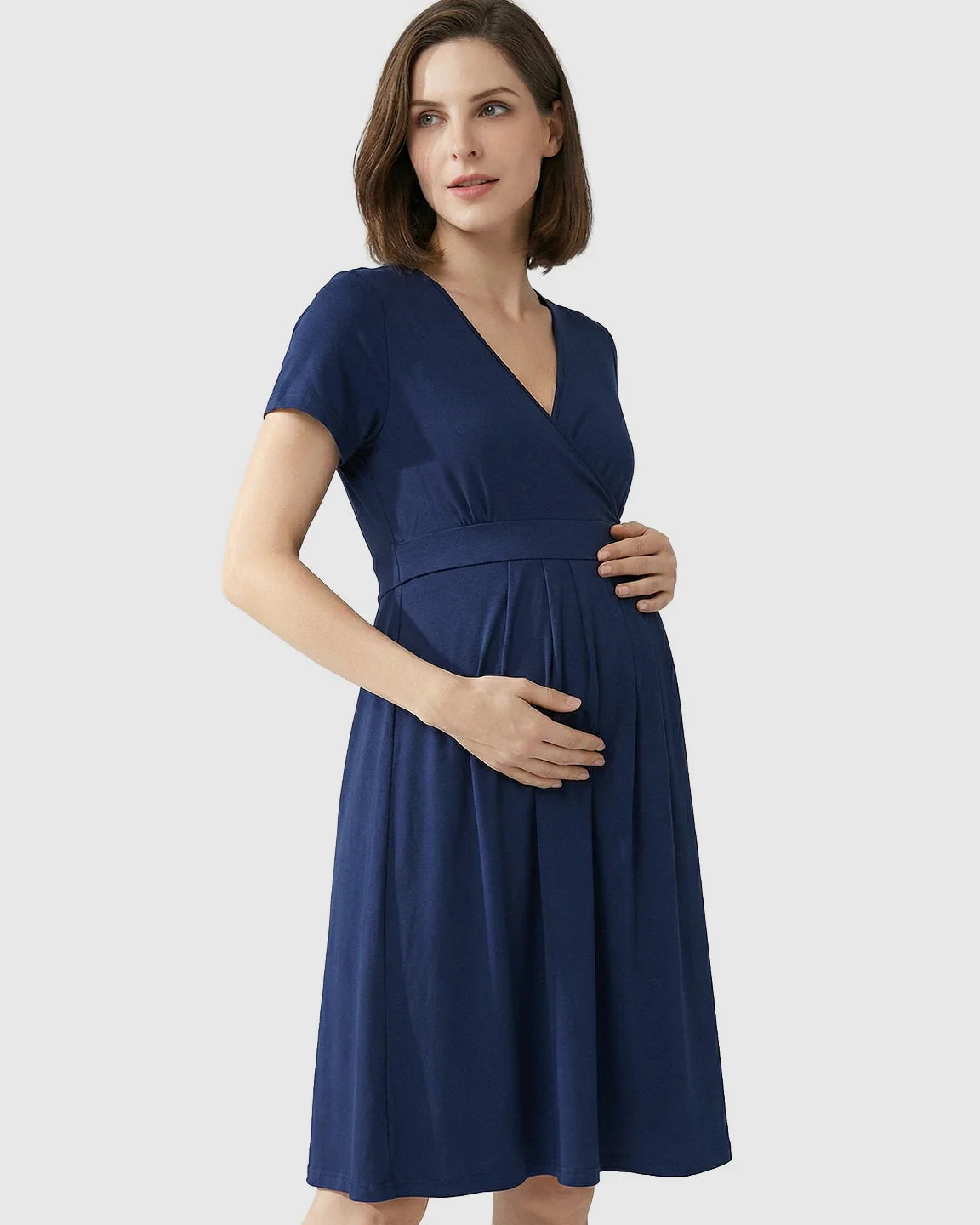 Pregnant woman in a navy blue V-neck A-line maternity and nursing dress, holding her bump.