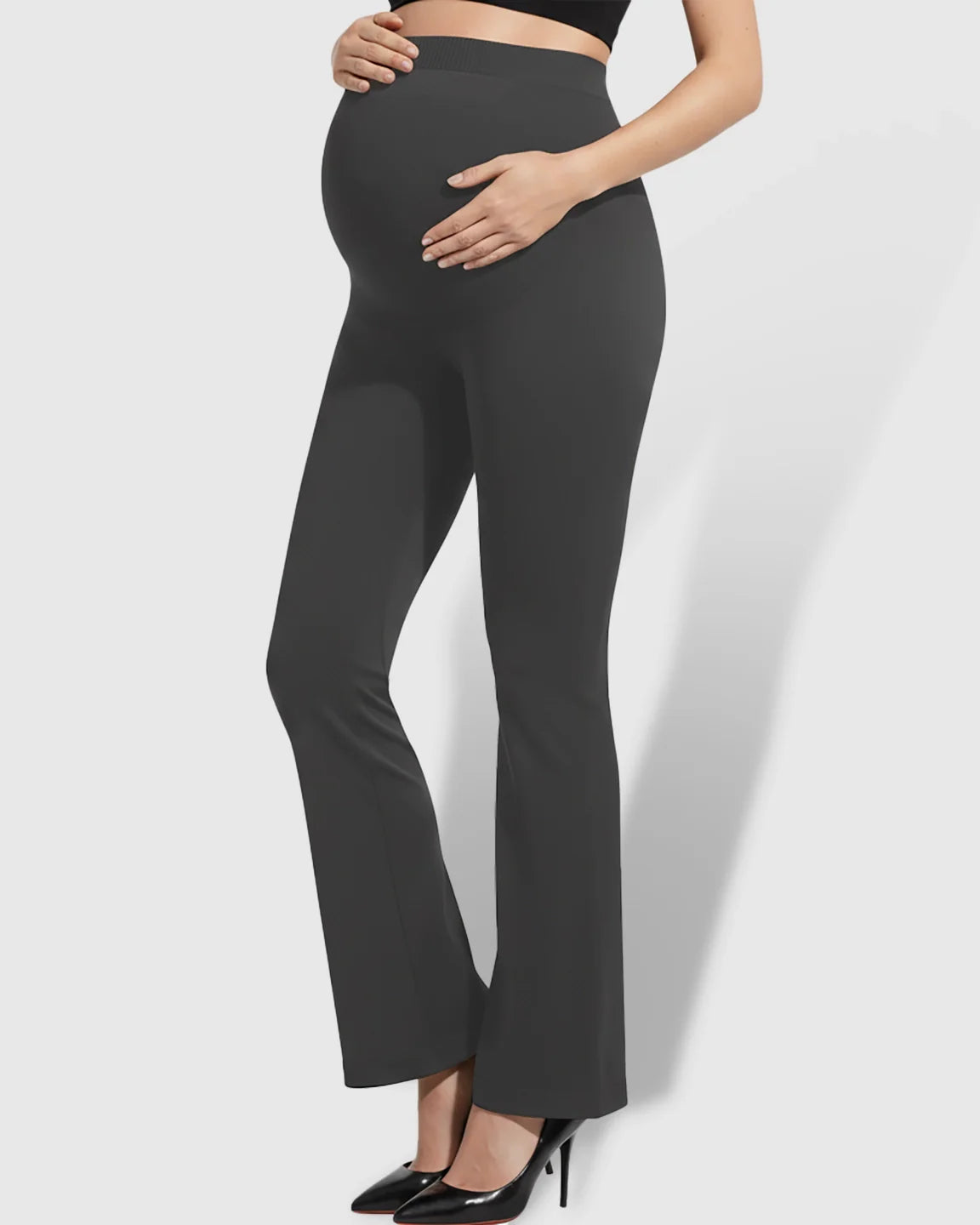 Maternity model in dark gray over-belly bootcut pants, supporting her bump.