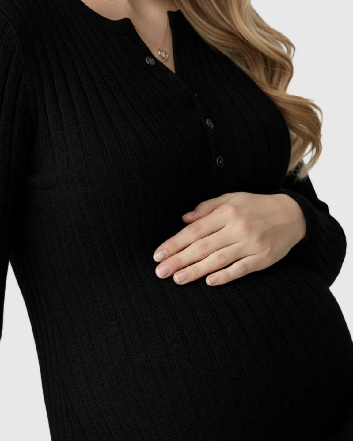 Pregnant woman in a black ribbed knit A-line long sleeve maternity maxi dress, gently holding her bump.