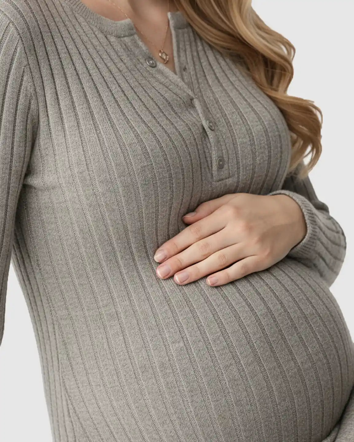 Pregnant woman in a gray ribbed knit A-line long sleeve maternity maxi dress, gently holding her bump.