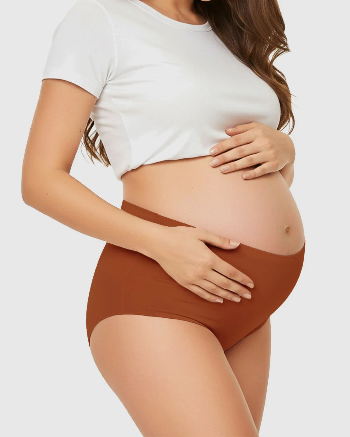 Pregnant woman in seamless high-waist terracotta maternity underwear, gently cradling her belly.