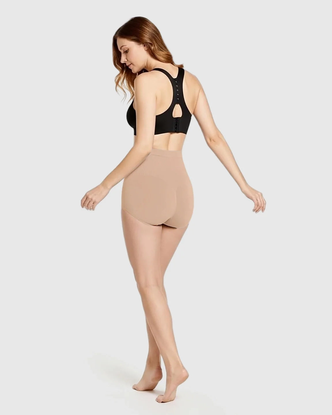 Woman from behind wearing nude high-waist seamless maternity panties and a black bra, showcasing the comfortable fit.
