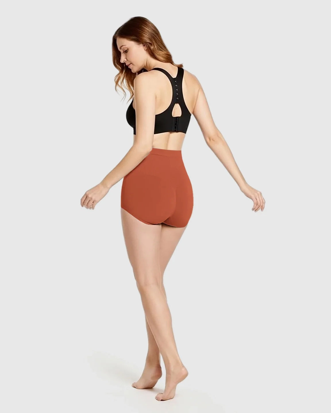 Woman modeling Bump Society high-waist seamless maternity panties in terracotta, paired with a black bra.