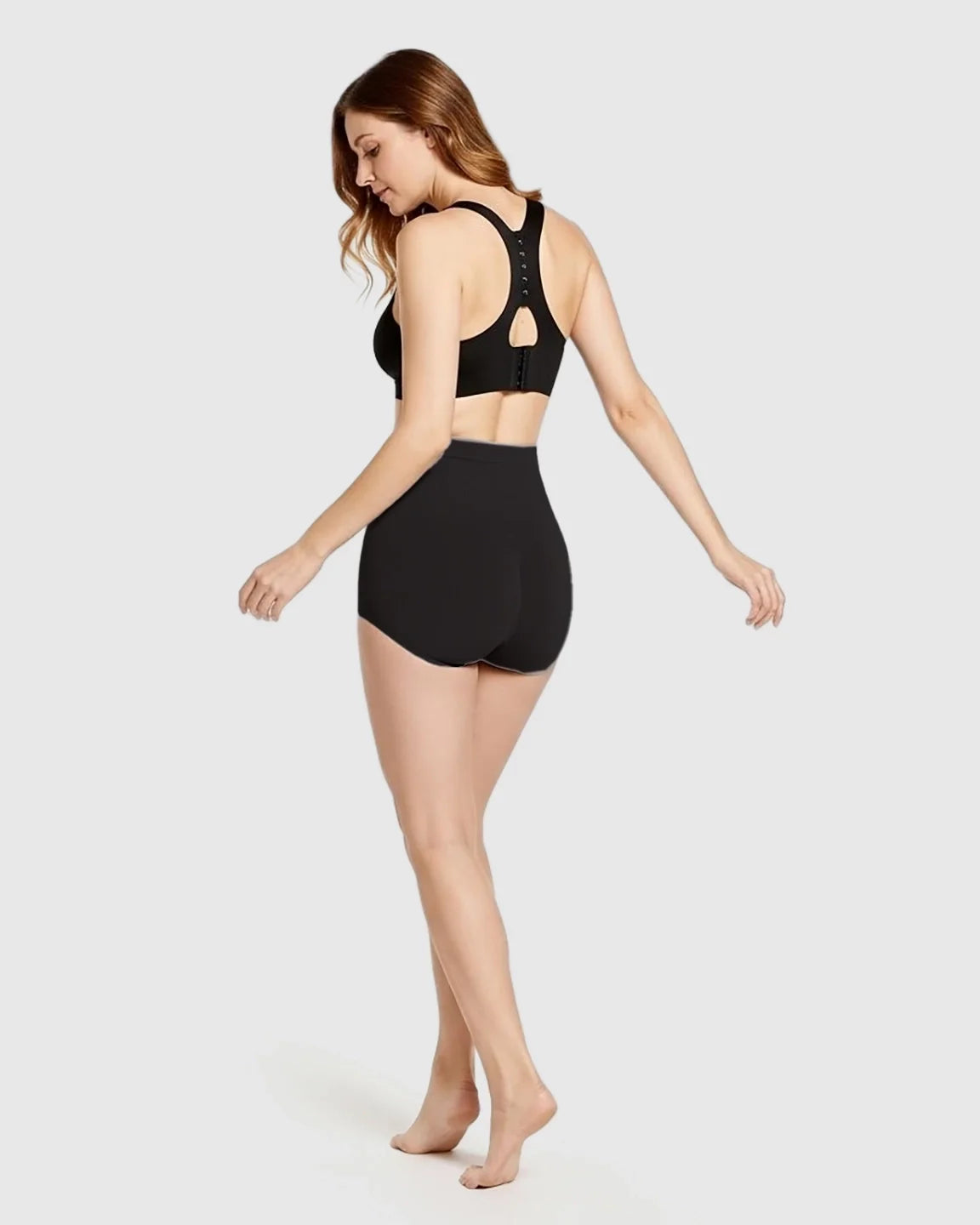 Woman from behind wearing black high-waist seamless maternity panties and a black bra.
