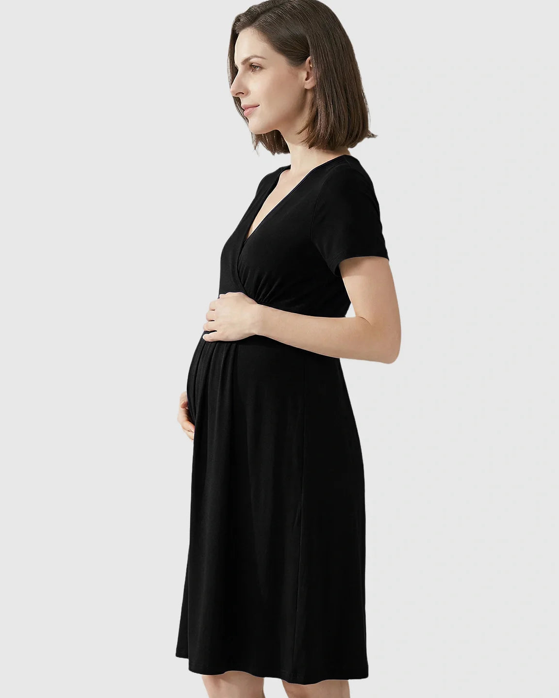 Pregnant woman in a black V-neck A-line maternity and nursing dress, holding her baby bump.